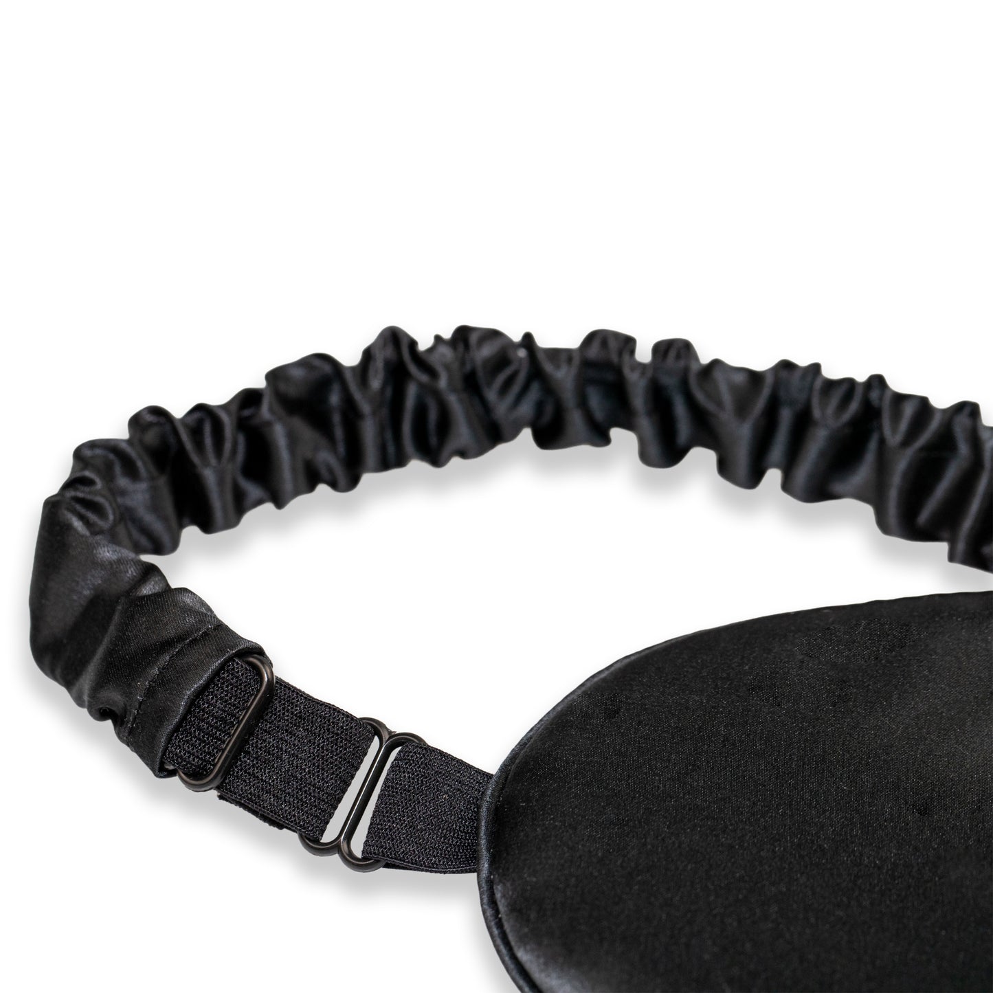 A close-up of a black SILKAVA silk sleep mask with an adjustable black elastic strap and metal slider buckle