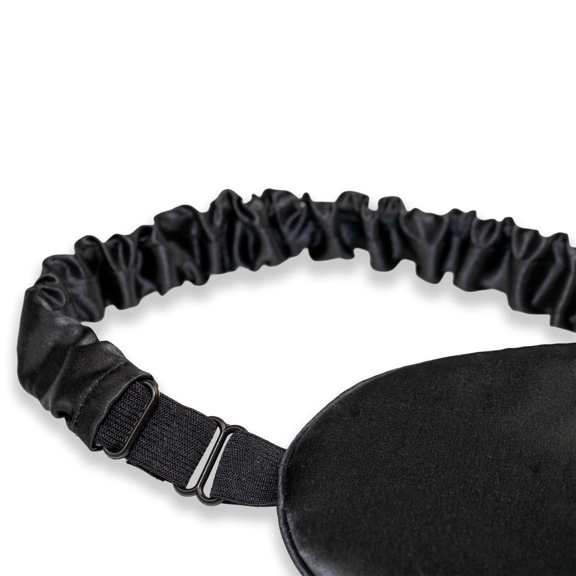 A close-up of a black SILKAVA silk sleep mask with an adjustable black elastic strap and metal slider buckle