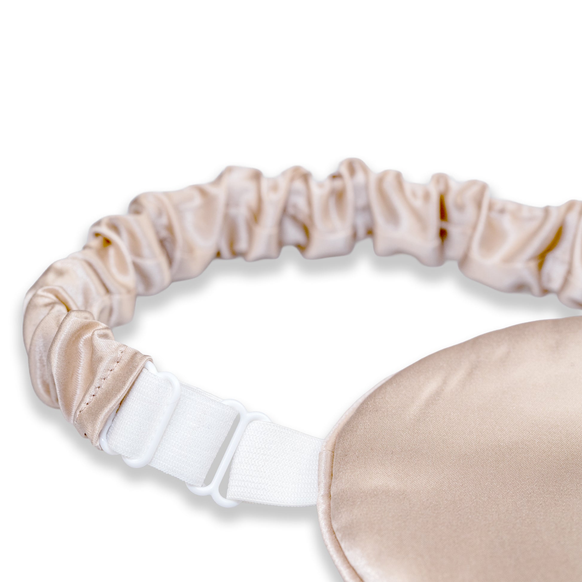 A close-up of a champagne SILKAVA silk sleep mask with an adjustable white elastic strap and metal slider buckle