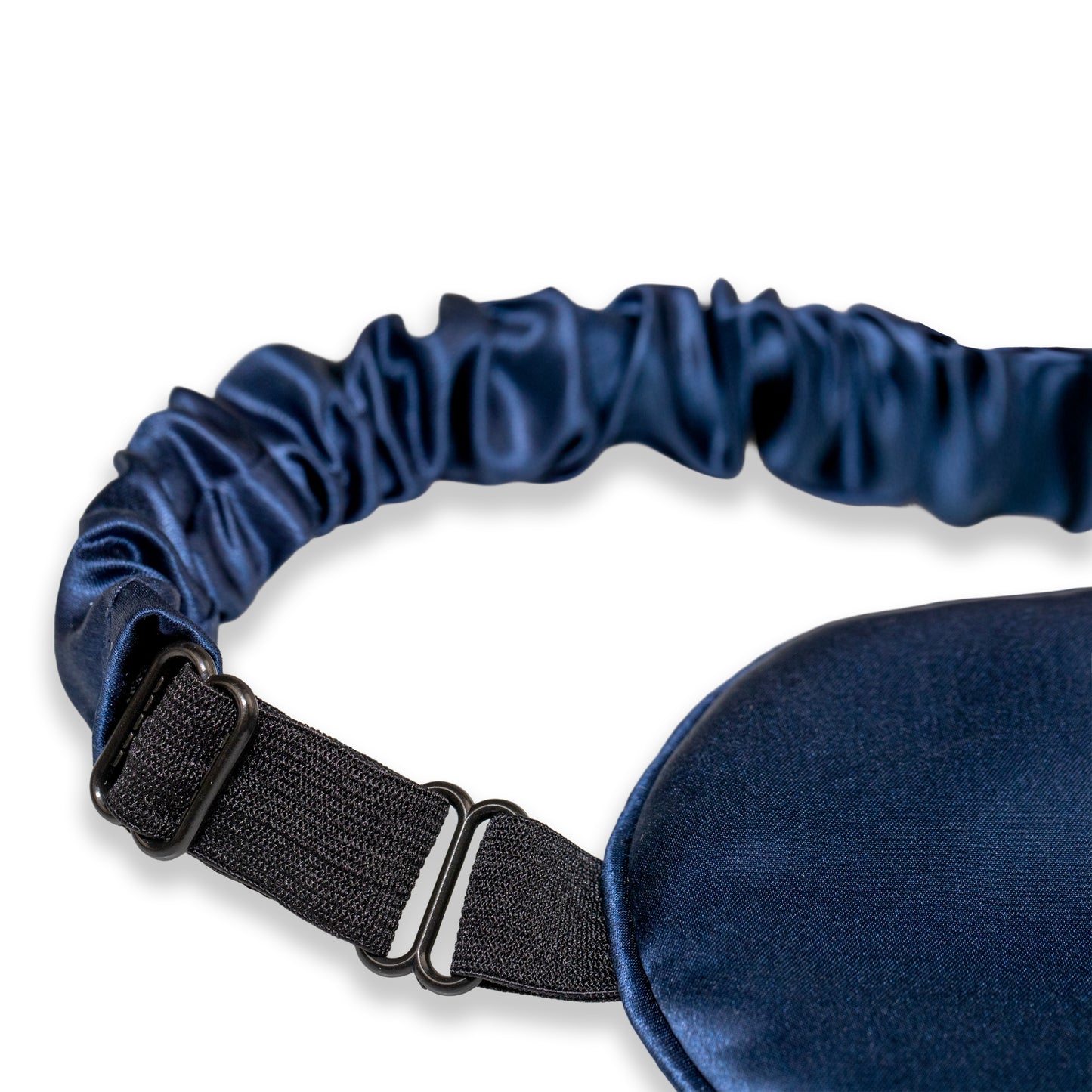 A close-up of a navy blue SILKAVA silk sleep mask with an adjustable black elastic strap and metal slider buckle